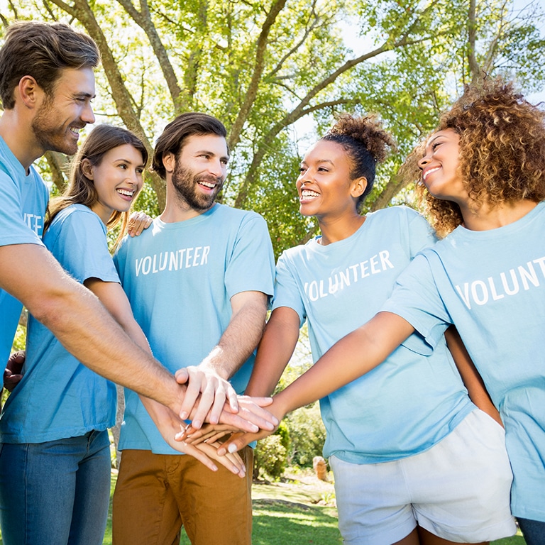 A group of volunteers wearing matching light blue t-shirts standing in a circle with their hands stacked together in the center.