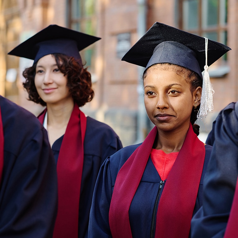 Group of students in graduation gowns standing outdoors and listening to lecturer